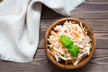 American ready-to-eat cole slaw salad of cabbage, celery, carrots and apple with basil leaves in a wooden plate and forks on a wooden table. Healthy and Eating Concept. Top view