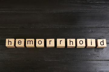 Wooden cubes with word HEMORRHOID on black table, top view