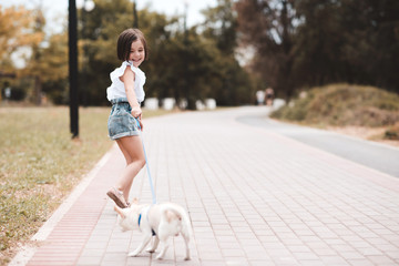 Fototapeta premium Funny baby girl 3-4 year old walking in park with puppy dog outdoors. Summer time. Childhood.