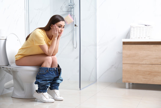 Upset woman sitting on toilet bowl in bathroom