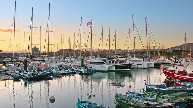 Las Galletas, Tenerife, Canary Islands - January 2019. Marina on the ocean. Luxury yachts moored in the bay. Sunset the sun's rays beautifully illuminate. Mountains and road in the background.