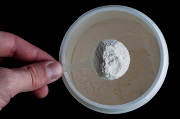Sports Nutrition Powder. Soluble creatine in a measuring spoon in the hand to increase muscle mass and strength. On a black background, isolate.