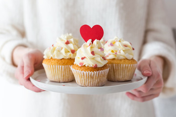 Valentine's Day. Sweet gift. Woman hands holding a plate with cupcakes decorated with hearts