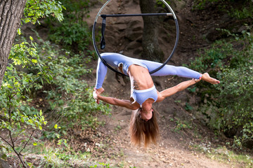 Aerial acrobat in a hoop. Young woman performs the acrobatic elements in the air ring. Outdoor shooting during the day.