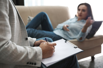 Professional psychotherapist and patient in office, focus on hands with clipboard