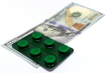 A plate of pills on a hundred dollar bill. Conceptual photo about the cost of drugs. Isolated on a white background.