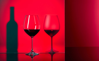 Bottle and glasses of red wine on a black reflective background.