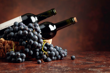 Juicy blue grapes and bottles of red wine on a brown background.