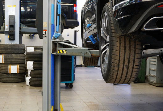 The luxury car at the service station is lifted to the lift. Concept of car service and seasonal tire change. The interior of the service and several rows of tires are blurry in the background.