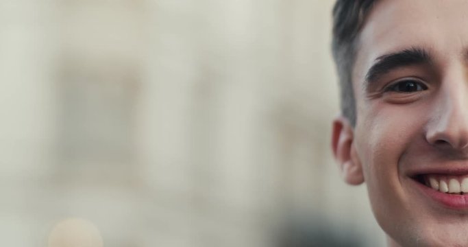 Close up of teh half face of the young Caucasian guy student with closed eyes, then boy opening his eyes and smiling happily to the camera. Outdoors.