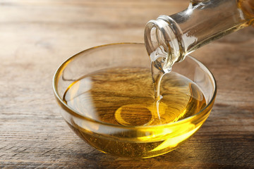 Pouring cooking oil from jug into bowl on wooden table
