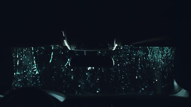 Drops flow down the windscreen. Inside view of a windshield car. Dark black cinematic picture. Process stage of polishing and washing a auto. Movement zoom camera dolly shooting platform.