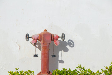 old red fire hydrant on a white wall in the sun