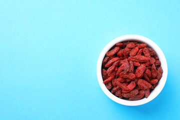 Dried goji berries in bowl on light blue background, top view. Space for text