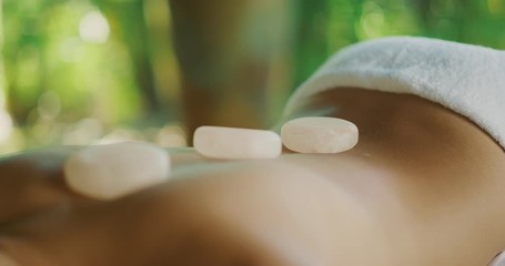 Attractive multi ethnic woman smiling content laying on a massage table with soothing hot crystal stones on her back, spa health and wellness concept, happy woman on vacation