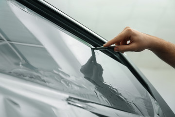Worker tinting car window with foil in workshop, closeup