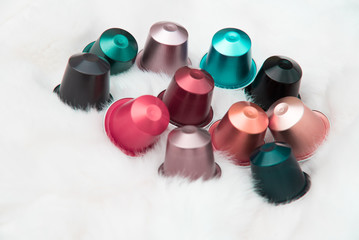 Colorful glossy coffee capsule group - abstract gathering of beautiful fashion pastel colors of aluminum pods on white fur or feather background - elegant watercolor cafe backdrop