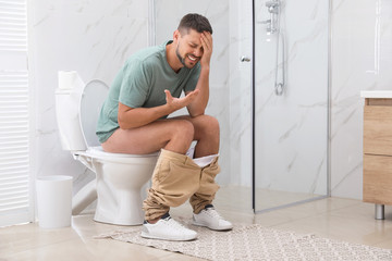 Man suffering from hemorrhoid on toilet bowl in rest room