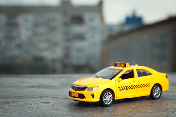 Fototapeta na wymiar Yellow taxi car model on city street. Space for text