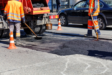 The group of road workers is repairing a section of the carriageway with fresh asphalt.