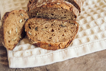 Brown fresh bread with seeds are cut into pieces on old wood background. Copy, empty space for text