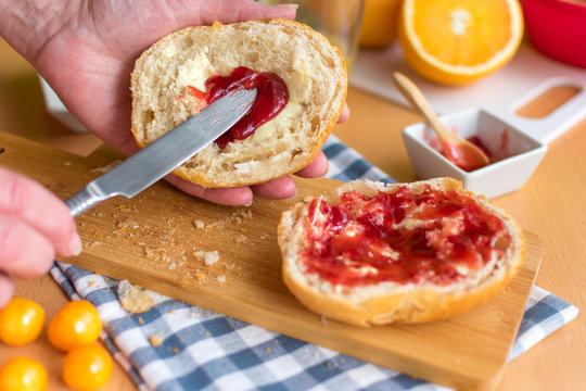 Hand streicht Erdbeermarmelade auf Br&ouml;tchen zum Fr&uuml;hst&uuml;ck