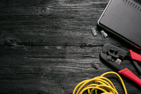 Computer network laying concept. Crimper tool, utp cable, net switch and connectors on black wooden table flat lay background with copy space.