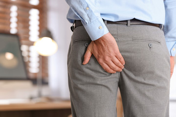 Man suffering from hemorrhoid in office, closeup