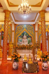Marble statue of a sitting Buddha in a richly adorned hall at Wat Chalong temple, located in Phuket, Thailand.