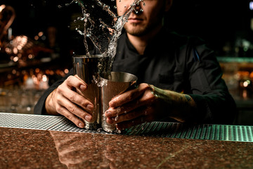 Male bartender holding in hands a steel shakers splashing the cocktail in it