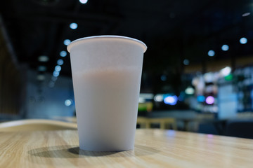 a white paper disposable coffee Cup stands on the table against the background of burning colored...