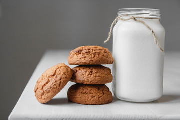 Milk in a glass jar and oatmeal cookies on a white table background. Copy, empty space for text