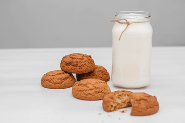 Milk in a glass jar and oatmeal cookies on a white table background. Copy, empty space for text