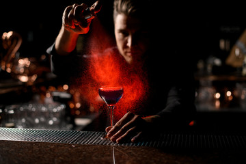 Professional bartender spraying on the blue alcoholic cocktail with a bitter under red light