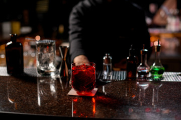 Professional male bartender serving the red alcoholic cocktail with ice cubes