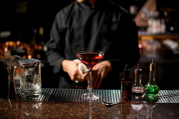 Professional male bartender serving the red alcoholic cocktail with ice cubes in the tall glass