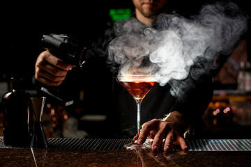 Professional male bartender serving the red alcoholic cocktail under the steam