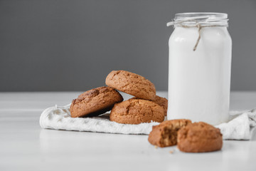 Milk in a glass jar and oatmeal cookies on a white table background. Copy, empty space for text