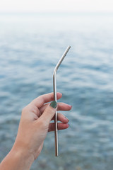Woman's hand holding a reusable steel drinking straw on sea background. Eco lifestyle and zero waste concept
