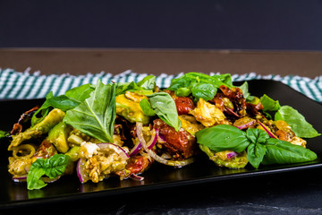Salad with avocado, sun dried tomato, red onion, feta and basil on plate on slate.