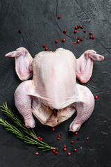 Raw whole chicken with rosemary and pink pepper. Black background. Top view