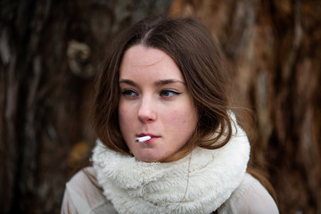 Smoking teenager in real life. Young beautiful white teeage girl in scarf smokes an cigarette near...