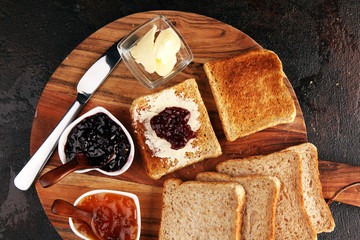 Toast bread with homemade strawberry jam and apricot marmalade on rustic table served with butter for breakfast or brunch on table