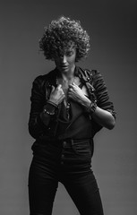 Young attractive sexy girl with curly hair in the form of a rock singer in a leather jacket. Black and white image