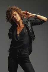 Young attractive sexy girl with curly hair in the form of a rock singer in a leather jacket