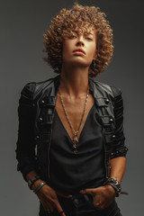 Young attractive sexy girl with curly hair in the form of a rock singer in a leather jacket