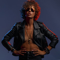 Young attractive sexy girl with curly hair in the form of a rock singer in a leather jacket