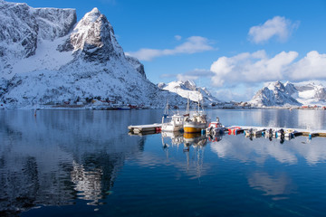 Naklejka premium Dock in the winter season. The background is a high mountain with snow and the reflection on the water. Reine, Lofoten Islands, Norway.