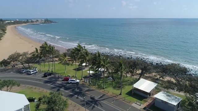 Aerial, green park with palm trees next to calm beach, pedestal up. Kellys Beach, Bargara, Australia.