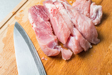 Cut pork meat into pieces with knife on cutting board.